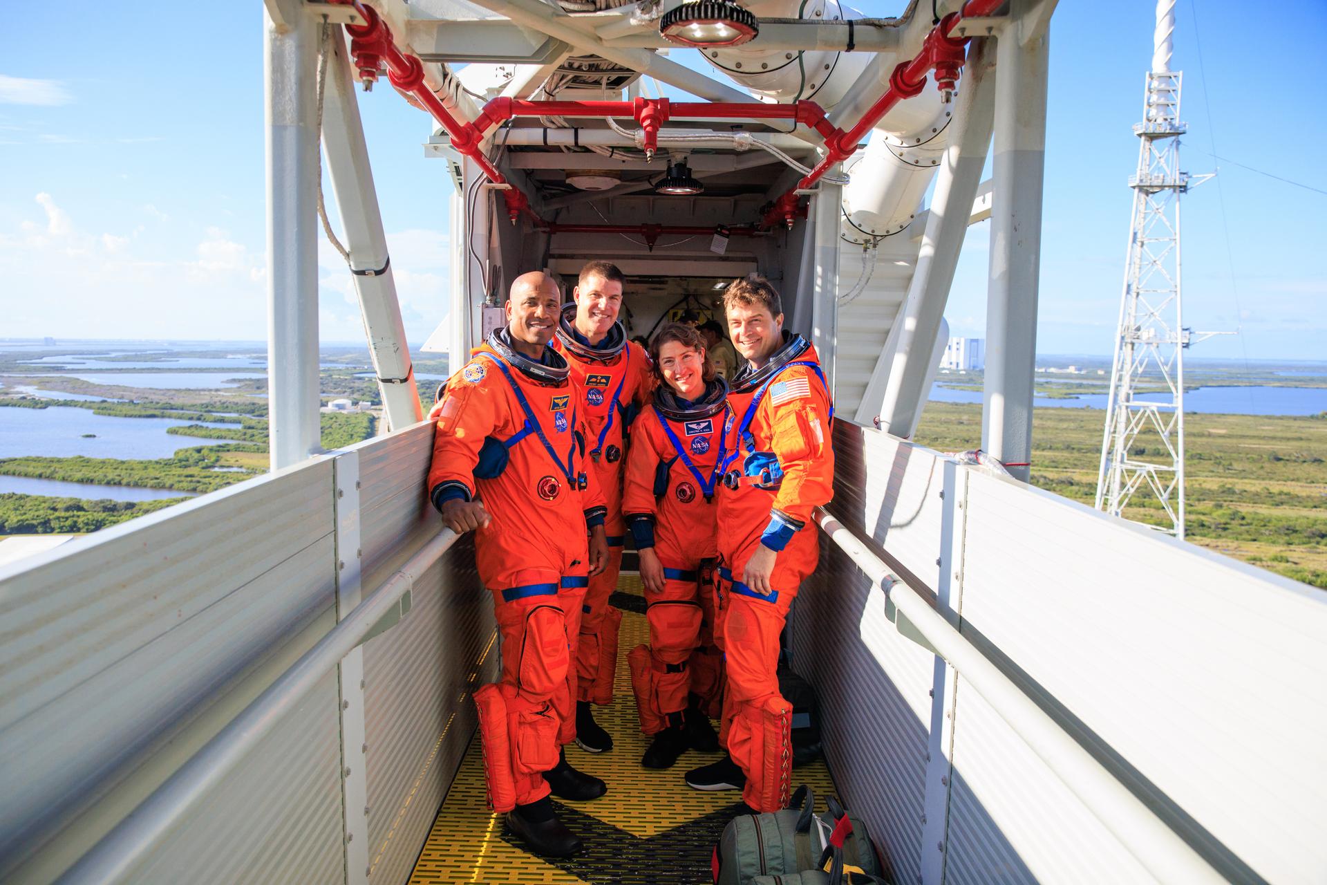 The Artemis II crew in orange launch and entry suits on the crew access arm.