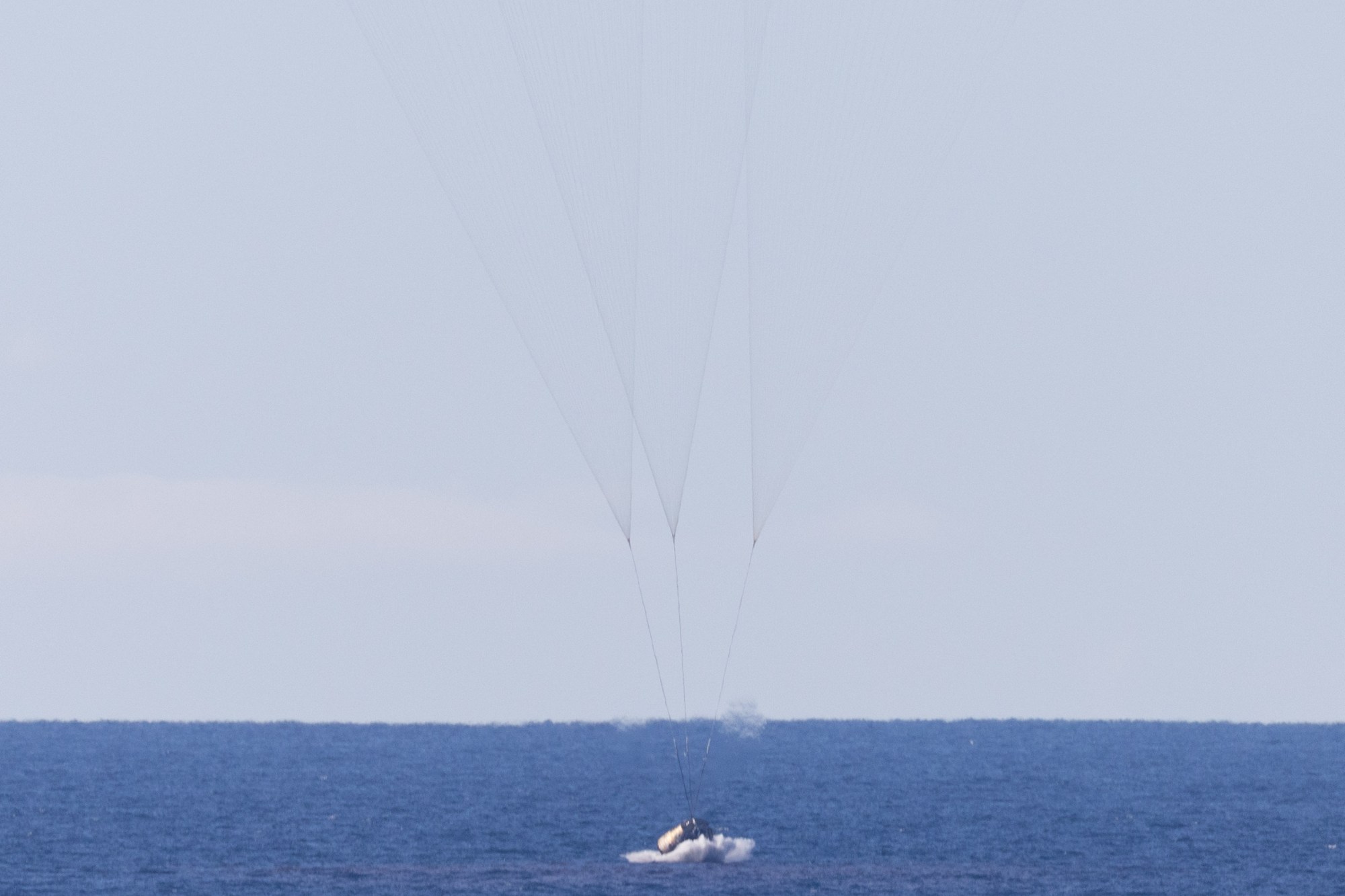 Orion splashing down in the Pacific Ocean under parachutes.